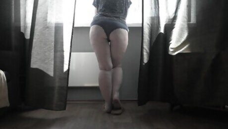 A mature housewife is standing in panties at the window.